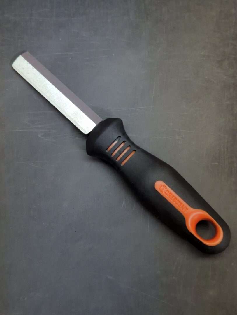 A Left-handed Knife with an orange handle on a black surface.